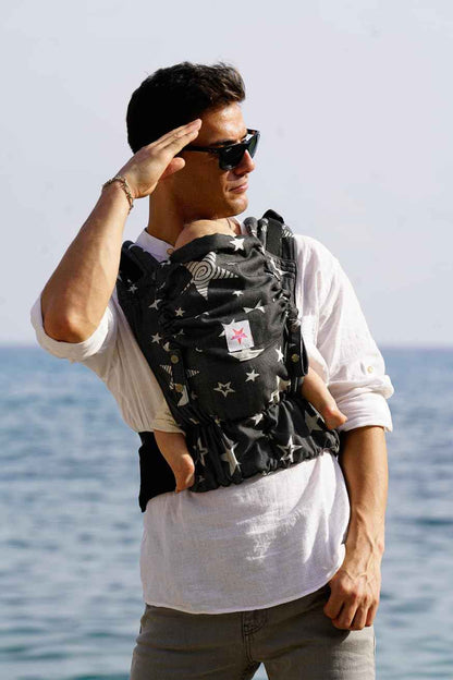 KOKADI Flip X Diorite Stars (Unisize)-Perfekte Kombi aus Fullbuckle & dem Tragen überkreuzt -Ab Geburt - 15 kg,handgefertigt aus 100%Bio-Baumwolle –Ergonomische Babybauchtrage Rückentrage Tragetasche